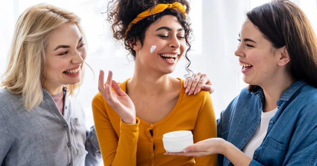 three beautiful ladies are laughing and applying cream on one lady 